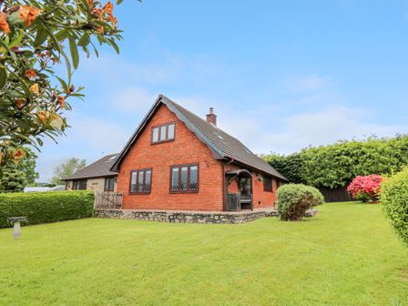 A brick house with a sloped roof and multiple windows surrounded by a green lawn and bushes at Pondarosa in Newbridge-On-Wye