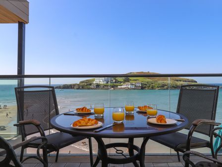 A balcony with a round table set with croissants and glasses of orange juice overlooking the beach and sea at 14 Burgh Island Causeway in Bigbury-On-Sea