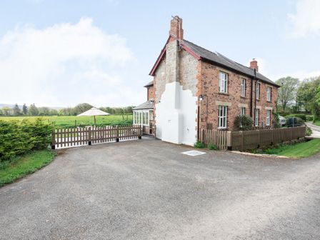 A brick house with a white chimney and brown fencing by a gravel driveway near green fields at 2 Siluria Cottage Walton near Kington