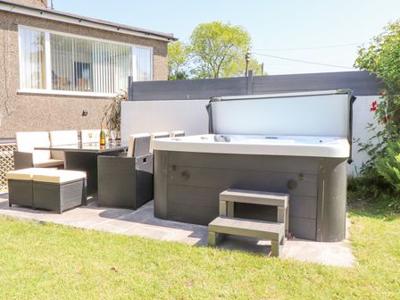 An outdoor patio area with a hot tub and a dining table with chairs at Tan Parc in Morfa Nefyn