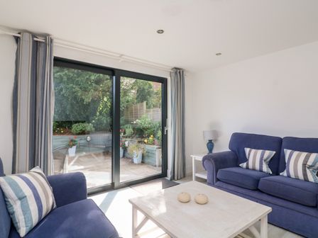 A living room with two blue sofas with striped pillows and a white coffee table near sliding glass doors at 1 Camperdown Lodge in Salcombe