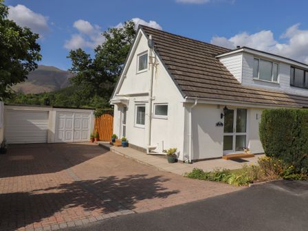 A driveway with potted plants in front of a white house with a tiled roof and a garage at Oaklea in Keswick
