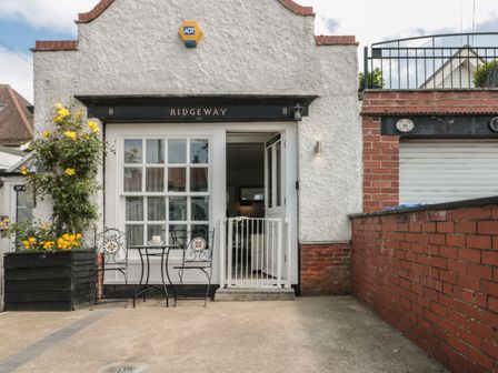 The exterior of a white building with a black sign reading Ridgeway and a patio area with two chairs and a table in Bridlington