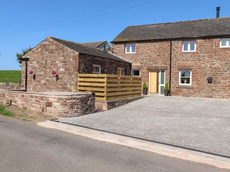 A stone house with a driveway a wooden fence and hanging flower baskets at The Granary in Allerby near Allonby