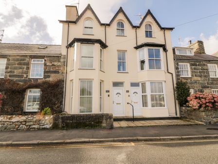 A street view of a cream colored building with two white doors and multiple windows at Bay View in Criccieth