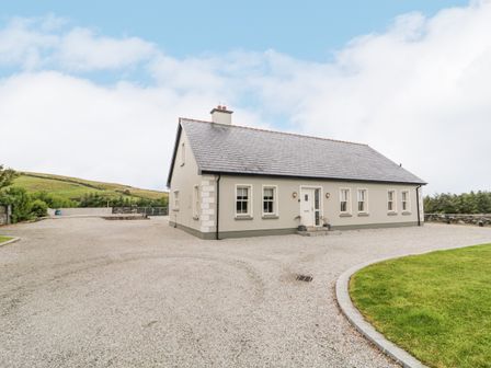 A single-story house with several windows and a front door surrounded by a gravel driveway and a lawn at Shroughan in Gortahork County Donegal