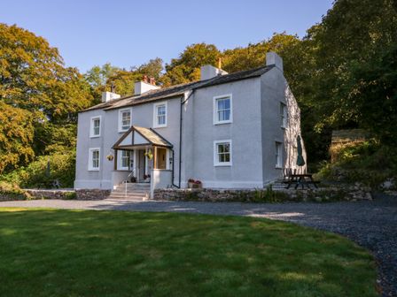 A two-story house with white walls surrounded by trees and grass at Dalegarth Hall Farm Cottage 1 in Boot near Eskdale Green