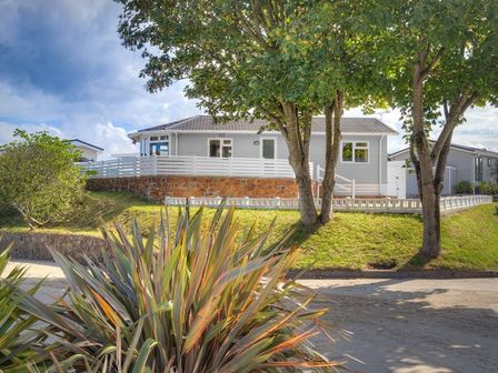 A raised house with a white fence and trees in front at E19 The Warren in Abersoch