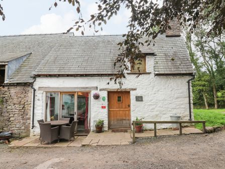 A stone cottage with a wooden door patio table and chairs and surrounding greenery at Ty Fferm Hen in Talybont-on-Usk