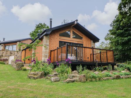 A wooden house with a deck and garden with flowers in front at The Bothy Riding Hills Riding Mill near Corbridge