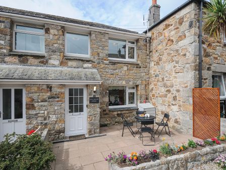 A stone cottage exterior with a small patio table and chairs and a flower bed at Wheal Charlotte Cottage in Perranuthnoe near Goldsithney