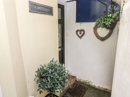 An entrance area with a black door a plant a doormat heart-shaped decorations and a sign 1 spetchley at Flat 1 Tenby