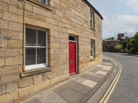 A stone building with a red door and windows along a curved street at White Feathers in Alnwick