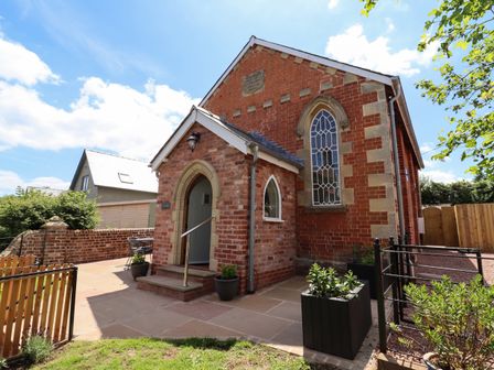 A brick building with arched windows and a small porch with steps surrounded by plants at The Old Chapel in Dorstone near Hay-on-Wye