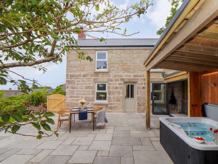 An outdoor patio with a dining table set for four and a hot tub under a wooden pergola at Carn House in Pendeen
