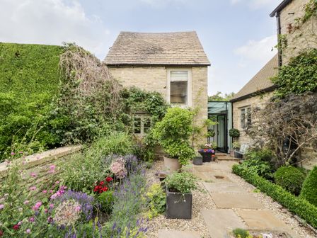 A garden path with potted plants and flowers leading to a stone house at The Grain Store in Ducklington near Witney
