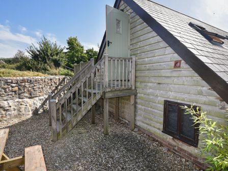 Exterior side view of a wooden house with a small staircase leading to an elevated door at Brookhaven in Musbury