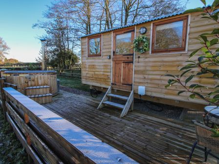 An outdoor wooden deck with a hot tub and a wooden cabin with a door and windows at The Oak Hut in Coton near Whitchurch