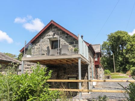 A stone house with a glass balcony and outdoor chairs surrounded by greenery at Stabal Bach in Criccieth