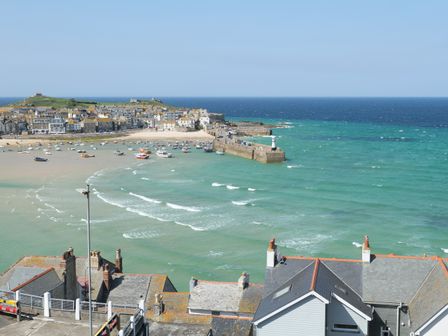 A coastal town with houses boats and a pier extending into the sea at Waves End in St Ives