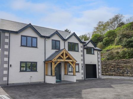 The front exterior of a two story house with black framed windows a wooden porch structure and an attached garage at Ty Mawr in Penrhyndeudraeth