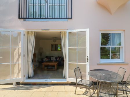 An outdoor patio with metal table and chairs outside open doors leading to a living room at 5 Combehaven in Salcombe