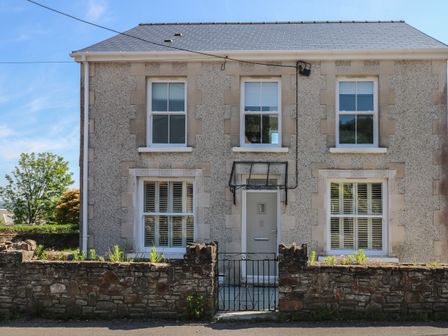 A two story house with four windows a front door and a stone wall with a gate at Gwynfryn in Pen-Clawdd