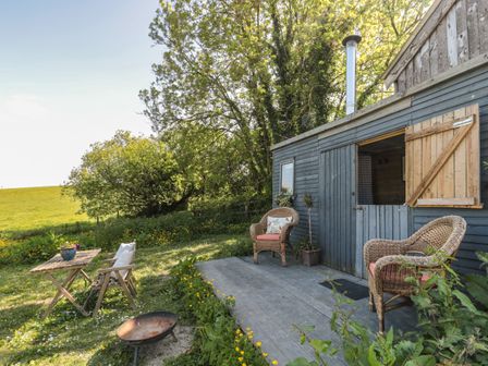 An outdoor seating area with wicker chairs and a wooden table next to a blue shed in a garden at The Snug in Dulverton