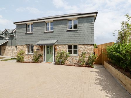 A two-story house with stone and shingle exterior a green door and paved driveway at Chynoweth House in Cubert