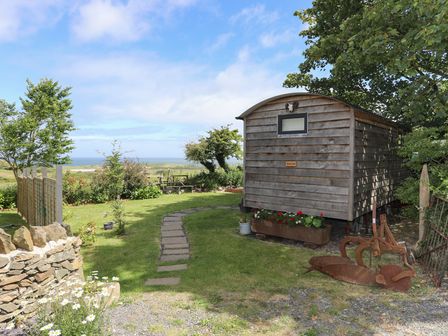 A garden area with a wooden shed flowers on the ground a stone wall and distant ocean view at Shepherds Stone Llanfairynghornwy near Llanfaethlu