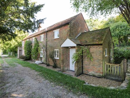 A brick cottage with white windows and a white door next to a dirt path and trees at Chalkpit Cottage in Blewbury