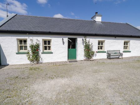 A white cottage with green door and window frames with a bench and climbing plants outside at Old Mikes Cottage in Westport County Mayo