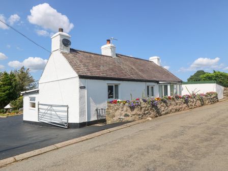 A white cottage with three chimneys and flower beds along a stone wall at Pen Bonc in Llanddaniel Near Gaerwen