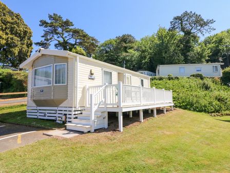 A beige mobile home with a white railing on a grassy slope with trees behind at Horizon in Combe Martin