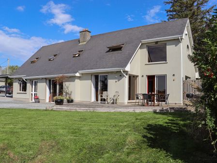 A modern two-story house with multiple windows and doors a patio with outdoor chairs and tables and a green lawn at Seafield in Ballymoney County Wexford