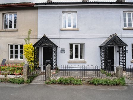 Two connected cottages with black doors and small front gardens at Hobbs Cottage in Sticklepath