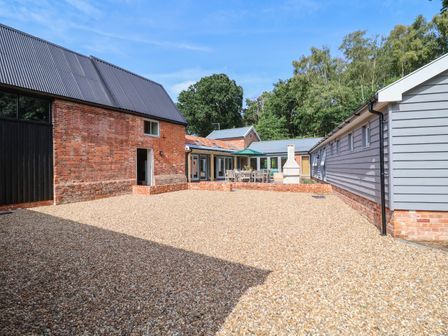 An outdoor courtyard with gravel floor surrounded by brick and wood buildings with tables and chairs in the background at Church Farm Barn Dunwich near Westleton