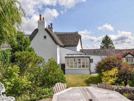 A garden with outdoor wooden furniture and bushes in front of a thatched cottage at Thatched Cottage in Charmouth