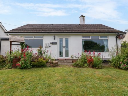 A small house with white walls and a tiled roof with a garden in front at Haul a Gwynt in Benllech