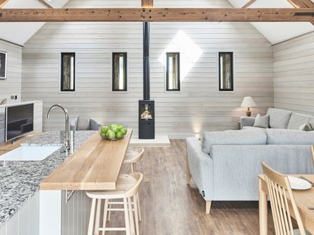 An open living space with a kitchen island with stools a sofa a wood burning stove and a dining table at The Hayloft in Humshaugh