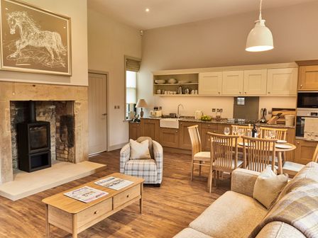 A living room with a fireplace a coffee table and a kitchen area with a dining table at The Stalls in Humshaugh