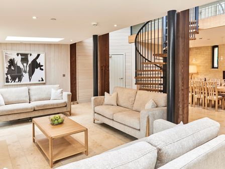 A living room with three sofas a wooden coffee table with green apples and a spiral staircase at The Clocktower in Humshaugh