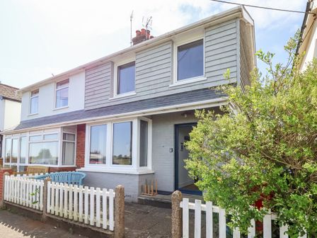 A semi detached house with white picket fence and green bushes at Long View in Southwold