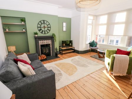 A living room with a gray sofa, green armchair, fireplace, wall clock, TV on stand, and wooden flooring at 36A Mary Street in Porthcawl