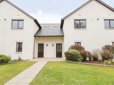 Entrance of residential building with two doors numbered 24 and 25 and a pathway leading to the doors with shrubs on the right and grass on the left at Whitbarrow 24 Penruddock