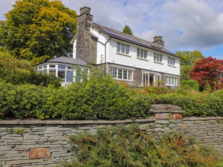 A two-story house with stone chimney and hedges in front at The Birches in Windermere