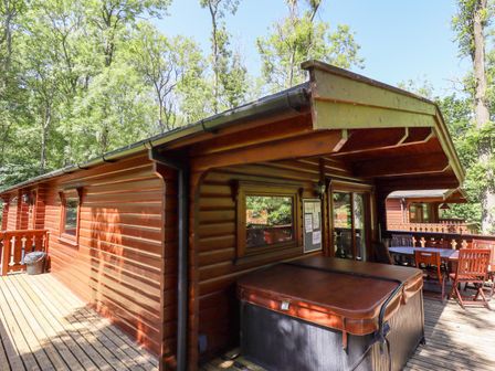 A wooden lodge with a covered porch featuring a hot tub and outdoor dining table surrounded by trees at 64 Acorn Lodge Kenwick Park in Louth
