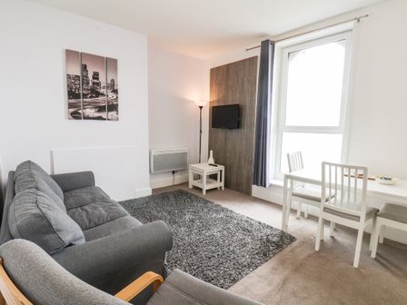 A living room with a gray sofa a gray armchair a white table with two chairs a floor lamp a wall-mounted TV and a large window at 8 Beach View Beaconsfield House in Bridlington