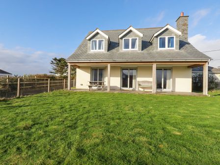 A house with a sloped roof and three dormer windows overlooking a lawn with a picnic table and bench at Freefolk in Polzeath