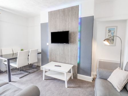 A living room with a wall mounted TV a white coffee table a grey sofa and dining table with white chairs at Ocean Wave in Bridlington